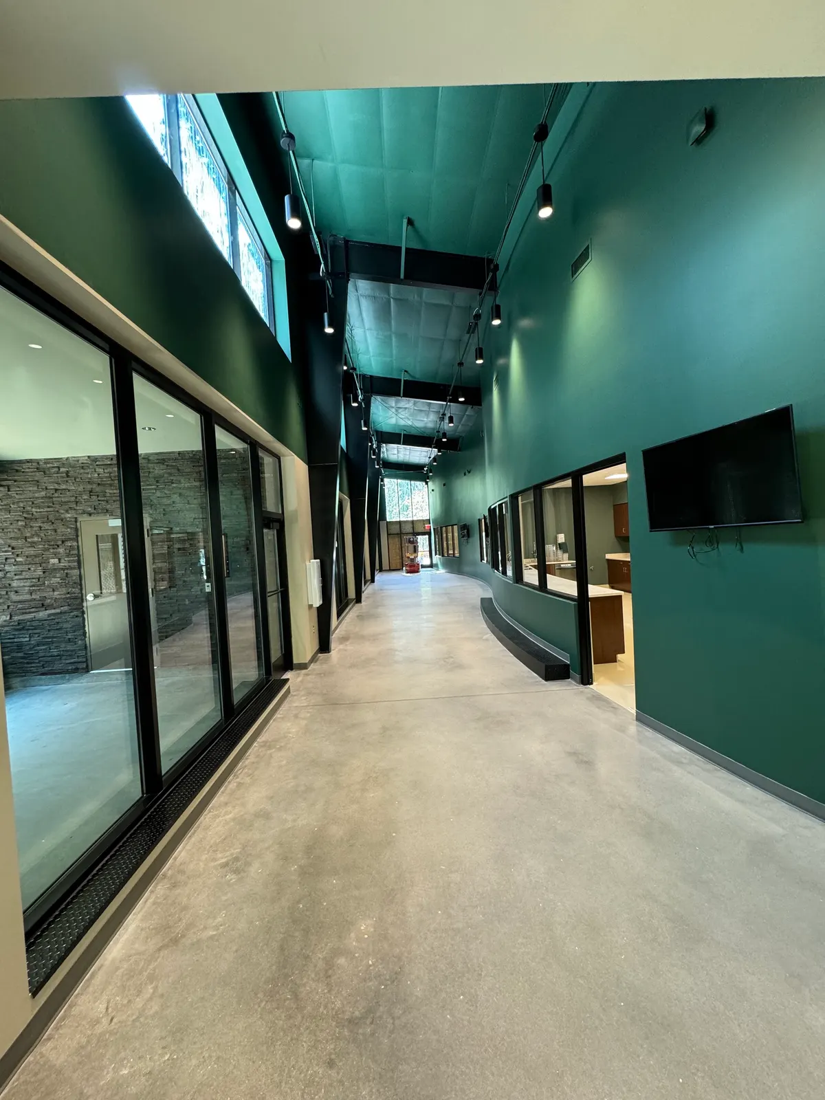 Long commercial corridor with teal walls and ceiling and glass storefronts