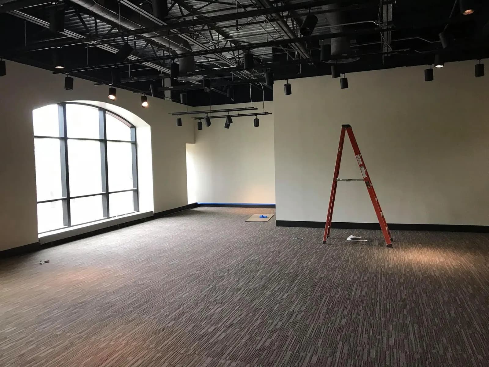 Large commercial room with white walls, an arched window and an open black ceiling